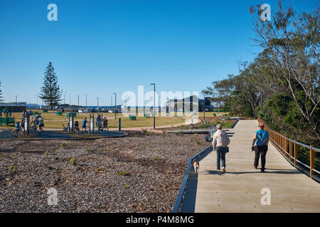 Due persone a piedi lungo un marciapiede al Jetty Foreshores Park su un luminoso cielo senza nuvole, Jetty Beach, Coffs Harbour, Nuovo Galles del Sud, Australia Foto Stock