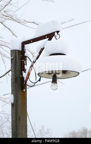 Un pilastro di legno con un lampadario. Il plafond della lampada è coperto con uno spesso strato di neve . Foto Stock