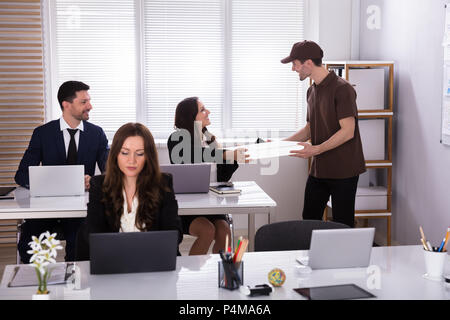 Felice imprenditrice ricevere la pizza dal giovane uomo di consegna in ufficio Foto Stock