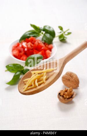 Gli Strozzapreti su un cucchiaio di legno con pomodoro, basilico e noci Foto Stock