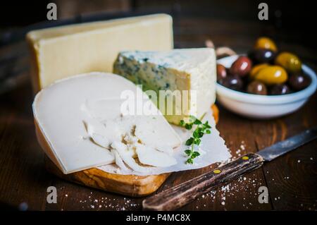 Vari tipi di formaggio su di un tagliere e un piatto di olive Foto Stock