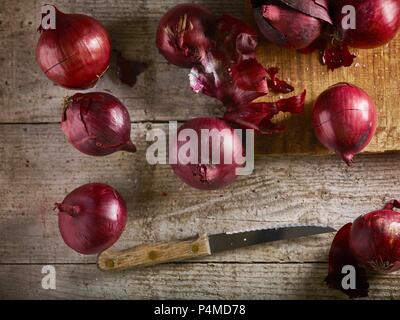 Le cipolle rosse sul tagliere e tavolo in legno con coltello Foto Stock