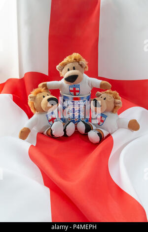 Tre Leoni sit in e intorno a una Inghilterra mug con un St George Cross bandiera come sfondo Foto Stock