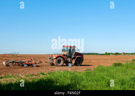 Grande trattore d'argento con un rosso disco erpice coltivatore in campo in una giornata di sole. Il concetto di lavoro in campi di agricoltura e industria. Foto Stock