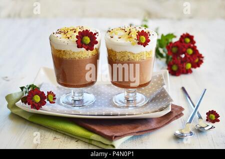 Il cioccolato, cereali e latte di cocco dessert in due bicchieri di servizio in piedi accanto a ogni altra e decorate con fiori freschi Foto Stock