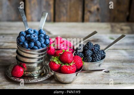 Frutti di bosco freschi in coppe d'argento su una superficie rustico Foto Stock