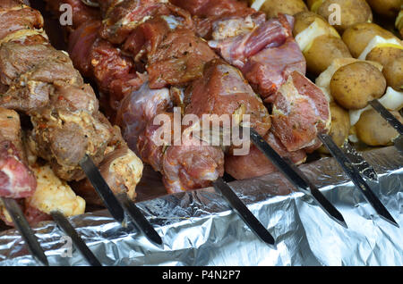 La carne cruda e le patate sono piantati su spiedini di metallo. Il processo di cottura shish kebab. Russo e ucraino cibo camp Foto Stock