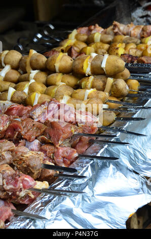 La carne cruda e le patate sono piantati su spiedini di metallo. Il processo di cottura shish kebab. Russo e ucraino cibo camp Foto Stock