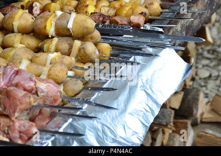 La carne cruda e le patate sono piantati su spiedini di metallo. Il processo di cottura shish kebab. Russo e ucraino cibo camp Foto Stock