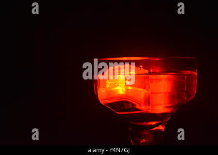 Splendida ed elegante foto di feste, celebrazioni, un bicchiere di champagne con cubetti di ghiaccio di plastica illuminati in bevande che illuminano la luce rossa. Foto Stock