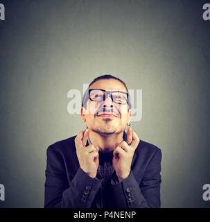 Giovani funny man in bicchieri tenendo le dita incrociate e gli occhi squinted rendendo nel contempo desidero su sfondo grigio Foto Stock