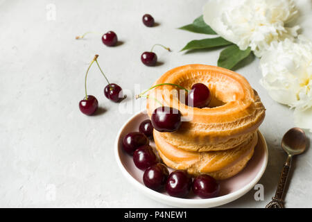 Torte di crema pasticcera anello con cherry su una piastra su un grigio sfondo a trama. Messa a fuoco selettiva Foto Stock