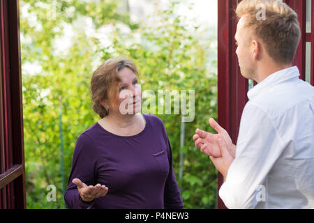 Vicini discutere la notizia, in piedi presso la recinzione. Una donna anziana parlando con un uomo giovane. Sono soddisfatto di questo incontro Foto Stock