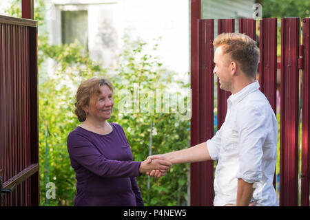 Vicini discutere la notizia, in piedi presso la recinzione. Una donna anziana parlando con un uomo giovane. Sono soddisfatto di questo incontro Foto Stock