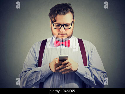 Barba eccentrico uomo d affari con red bow tie in bicchieri utilizzando uno smartphone Foto Stock