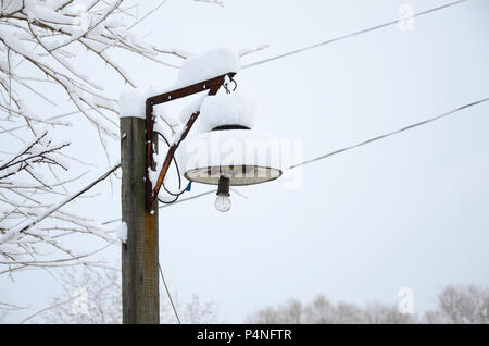 Un pilastro di legno con un lampadario. Il plafond della lampada è coperto con uno spesso strato di neve . Foto Stock