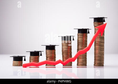 Aumentando la freccia rossa nella parte anteriore delle monete impilate con graduazione Hat su sfondo bianco Foto Stock