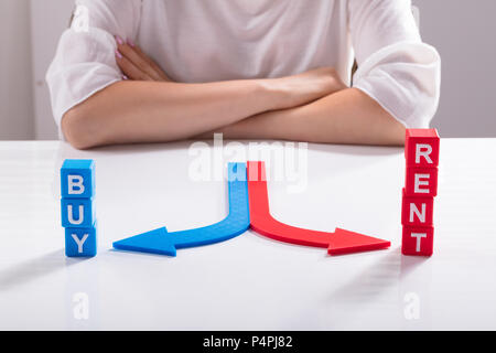 Il rosso e il blu delle frecce che indicano i blocchi cubici con noleggiare e acquistare le direzioni sulla scrivania Foto Stock