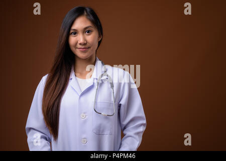 Giovane bella donna asiatica medico contro sfondo marrone Foto Stock