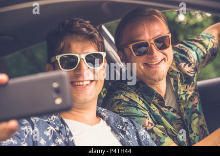 Hipster moda ragazzi seduti in auto e tenendo selfie con smart phone. Foto Stock