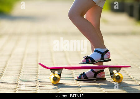 Bambino gambe slim in calze bianche e sandali nero sulla plastica rosa su skateboard luminosa estate copia sfocata spazio sullo sfondo della pavimentazione. All'aperto ac Foto Stock