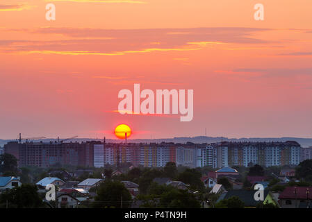 Bellissima alba nella periferia della città. Grande e luminosa il bianco e il giallo del sole più alto edificio di appartamenti, lavorando gru a torre e tetti di case tra il verde di tre Foto Stock