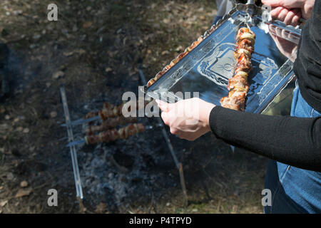 Una donna è in possesso di un vassoio con un shish kebab. Barbecue all'aperto il concetto di partito. Inizio giornata di primavera. Sfondo di carne. Vista laterale. Foto Stock