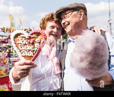 Ritratto di felice coppia senior con cuore di panpepato e cotone candy sul fair Foto Stock