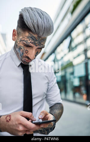 Giovane imprenditore con tatuato faccia utilizza lo smartphone Foto Stock