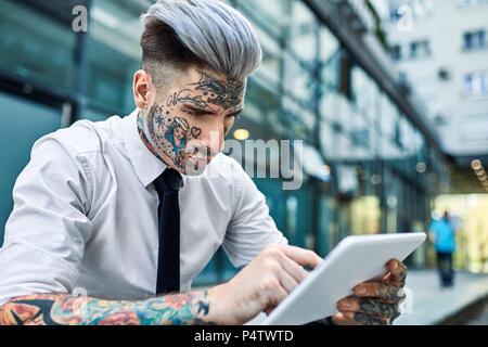 Giovane imprenditore con tatuato faccia, con tavoletta digitale Foto Stock