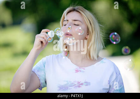 Giovane donna bionda che soffia bolle di sapone all'aperto Foto Stock