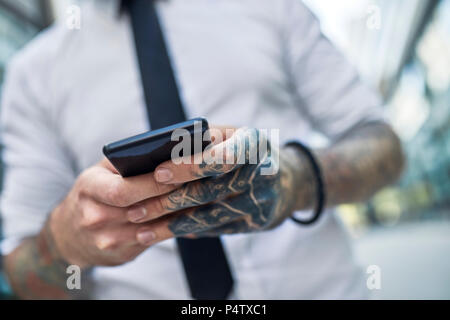 Giovane imprenditore con tatuato faccia utilizza lo smartphone Foto Stock