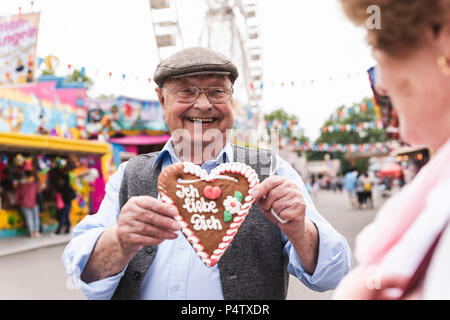 Ritratto di felice senior uomo presentando gingerbread cuore sul fair Foto Stock