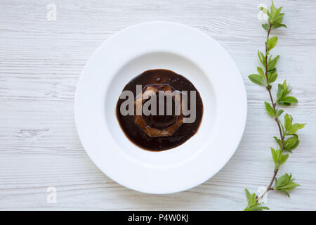 Panacotta dessert con cioccolato in piastra di bianco su bianco sullo sfondo di legno decorate con la fioritura del ramo di ciliegio. Lay piatto. Vista dall'alto. Da sopra. Foto Stock