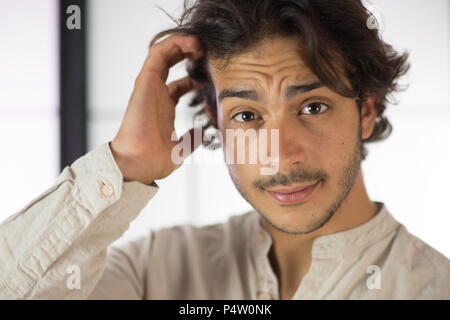 Un bel giovane uomo, 20Y, è in posa di studio di graffiare i suoi capelli in un ragionato pongono. Il cappello in primo piano. Sfondo nero. Foto Stock