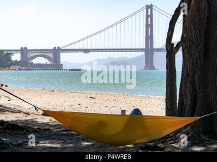 Persona stabilisce in amaca durante la lettura del libro con il Golden Gate Bridge a distanza Foto Stock