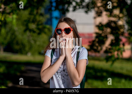 Ragazza schoolgirl in estate in città. In calici a forma di cuore dietro lo zaino. Il concetto di sorpresa sorpresa sorpresa. Emozione sorpresa sorpresa regalo. Foto Stock