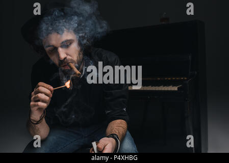 Bello barbuto musicista di fumare il sigaro nella parte anteriore del piano su nero Foto Stock