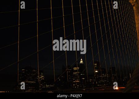 Stati Uniti. New York. Vista notturna di Manhattan attraverso le bretelle del ponte di Brooklyn. Foto Stock