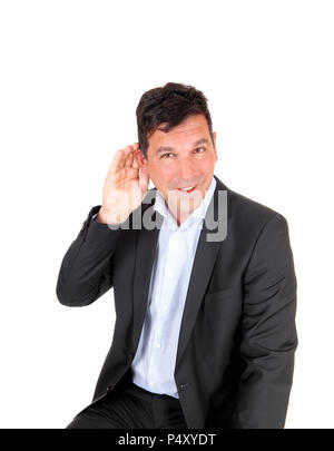 Un uomo bello ha problemi di udito, tenendo la sua mano dietro il suo orecchio, seduta in una tuta, isolato per sfondo bianco Foto Stock