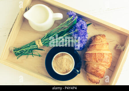 Tazza di caffè espresso con croissant fresco, latte e bouquet di cornflowers blu sul vassoio in legno Buona mattina concetto. Godetevi la vita lenta. Giorno di estate ro Foto Stock