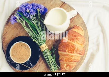 Romantico in estate la colazione a letto, vassoio con croissant freschi, una tazza di caffè espresso con il latte e bouquet di cornflowers blu. Buona mattina concetto. E Foto Stock