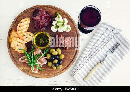 Antipasti italiani vino snack set. Mozzarella, Mediterraneo olive, Prosciutto di Parma, la bresaola, pomodori secchi e brindisi sulla boa in legno Foto Stock