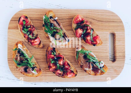 Selezione di gustosi italiano bruschette o tartine su baguette tostato condito con pomodoro, Prosciutto di Parma, rucola e balsamico salsa glasse su c Foto Stock