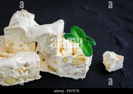 La deliziosa e tradizionale festa italiana torrone torrone o con i dadi sulla pietra nera dello sfondo. Torrone morbido blocchi con mandorle con foglie di menta fresca. H Foto Stock