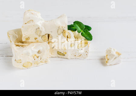 La deliziosa e tradizionale festa italiana torrone torrone o con i dadi su bianco sullo sfondo di legno con posto per il testo. Torrone morbido blocchi con mandorle con Foto Stock