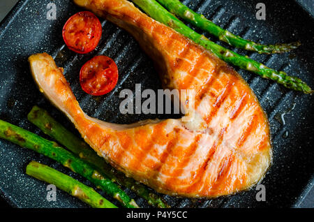 Salmone alla griglia bistecche, gli asparagi e i pomodori ciliegia preparato in padella per grigliare su pietra nera dello sfondo. Cibo sano concetto. Close up. Vista dall'alto. Foto Stock