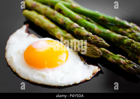 Uovo fritto e arrosto di asparagi freschi nella piastra nera. Pranzo sano concetto. Deliziosi e nutrienti mangiare. Foto Stock