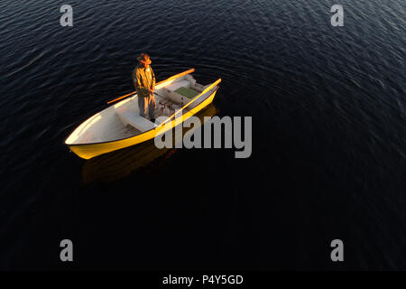 Lulea, Svezia - 16 Giugno 2018: un uomo e il suo cane in piedi in una barca a remi la pesca al tramonto. Foto Stock