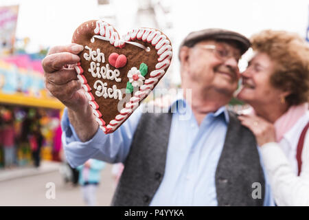 Mano di uomo senior holding ingerbread cuore sul fair, close-up Foto Stock